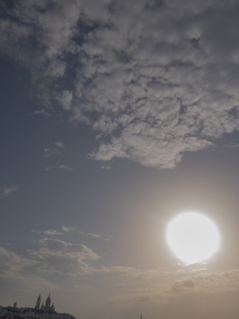 Une photo où le soleil paraît énorme, trop près de la Terre pour qu'elle soit vivable et où une distorsion donne l'impression que le Sacré Coeur se tend vers les nuages."Il fait chaud".