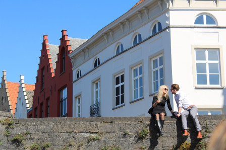 Un couple d'amoureux assis sur un pont et vus d'un bateau sur le canal, à Bruges.