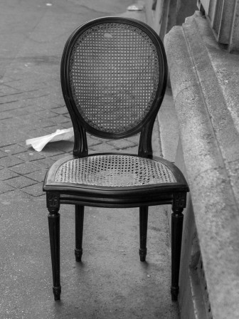 Une chaise un peu trop usée abandonnée sur un trottoir parisien.