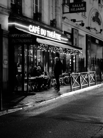 Un homme parle avec des gens en train de prendre un café en terrasse, ce matin, en bas du bureau. Version N&B.