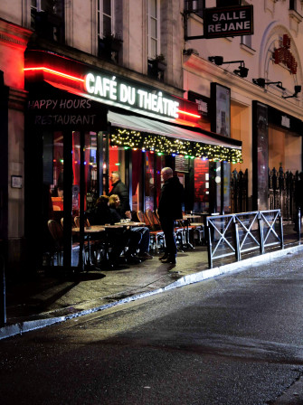 Un homme parle avec des gens en train de prendre un café en terrasse, ce matin, en bas du bureau. Version couleurs.