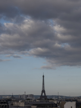 La tour Eiffel sur un ciel bleu, et sous des nuages dont les teintes vont du blanc au gris.
