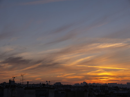 Le ciel bleu et en nuances d'oranges, du doux au flamboyant, à l'heure où le soleil a passé l'horizon. La silhouette de Paris se détache, très sombre, à peine reconnaissable, en bas.