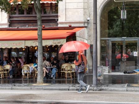 Un homme au parapluie rouge assorti au café devant lequel il passe.