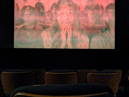 Une salle de cinéma, quelques sièges vides et un écran sur lesquels des visages sont projetés (apeurés ? inquiets ? surpris ?)